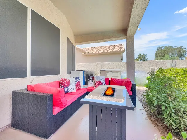 Patio lounge with a wicker sectional, red cushions and a lit fire table