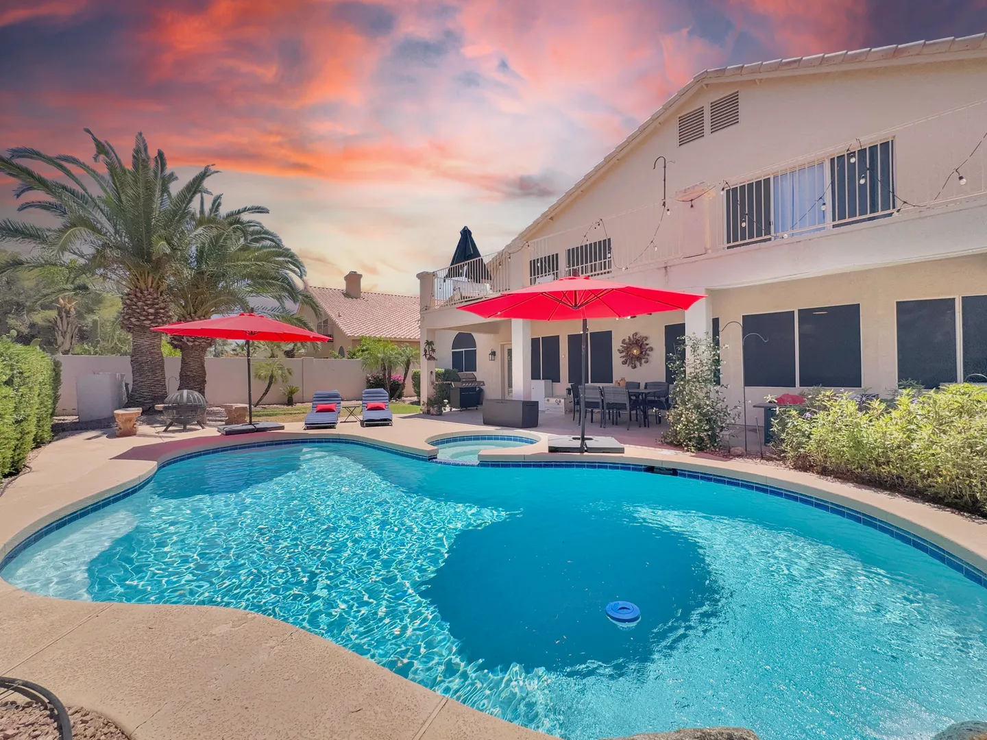 Private pool and spa in the backyard, with palm trees, a red patio umbrella and the two-story house behind